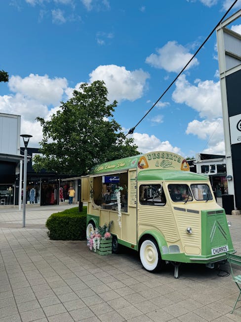 The image shows the exterior of a modern shopping centre with large glass windows and a curved architectural structure under a cloudy sky. Multiple pedestrians are walking along the paved pathway outside, including a man and woman engaged in conversation, a young child holding hands with an adult, and others passing by, some with shopping bags. Inside the shopping centre, partially visible through the glass, are signs of retail spaces such as a Foodies store, with a wooden display stand positioned near the entrance. The scene captures a typical busy day with shoppers, and the area appears well-lit with natural daylight. This setting relates to house removals and furniture transport, reflecting the logistical process of relocating household items through professional services like those offered by Man and Van Brent Cross, which handle packing and moving logistics for residents in the Brent Cross area.